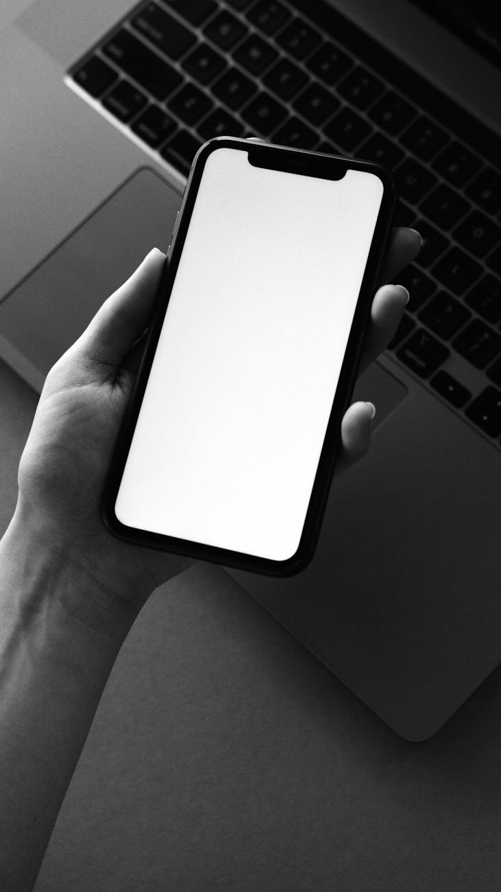 Monochrome photo of a smartphone held over a laptop for tech-themed design.