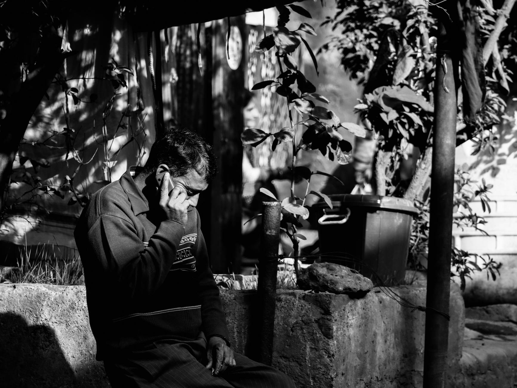 A thoughtful man talking on a mobile phone in a moody grayscale street scene.