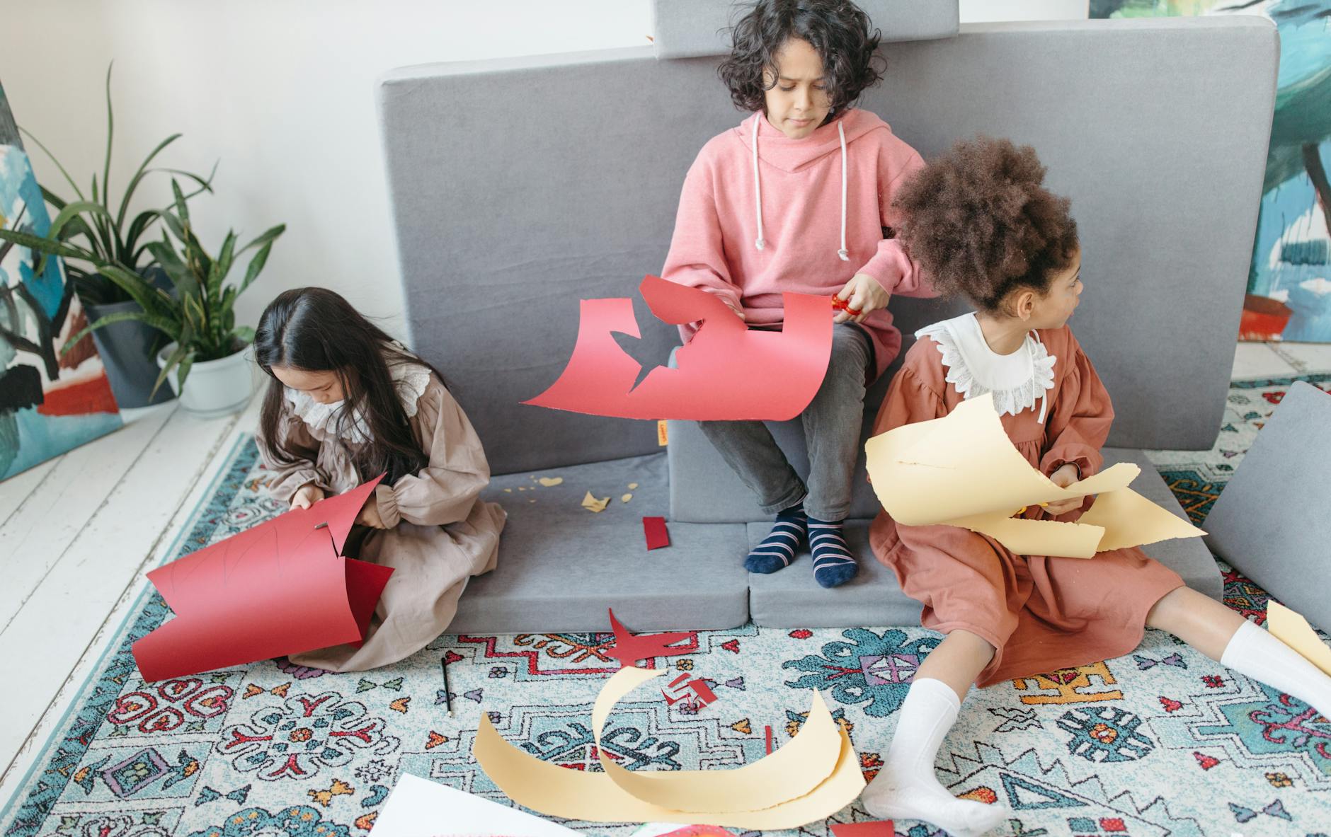 Three children sitting indoors, cutting colorful paper for a school art project.