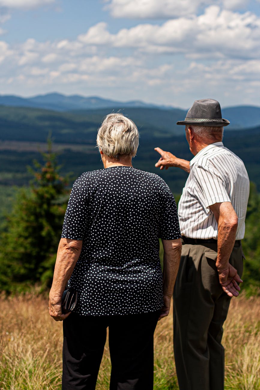 Senior couple standing together, admiring a stunning mountain landscape on a sunny day.