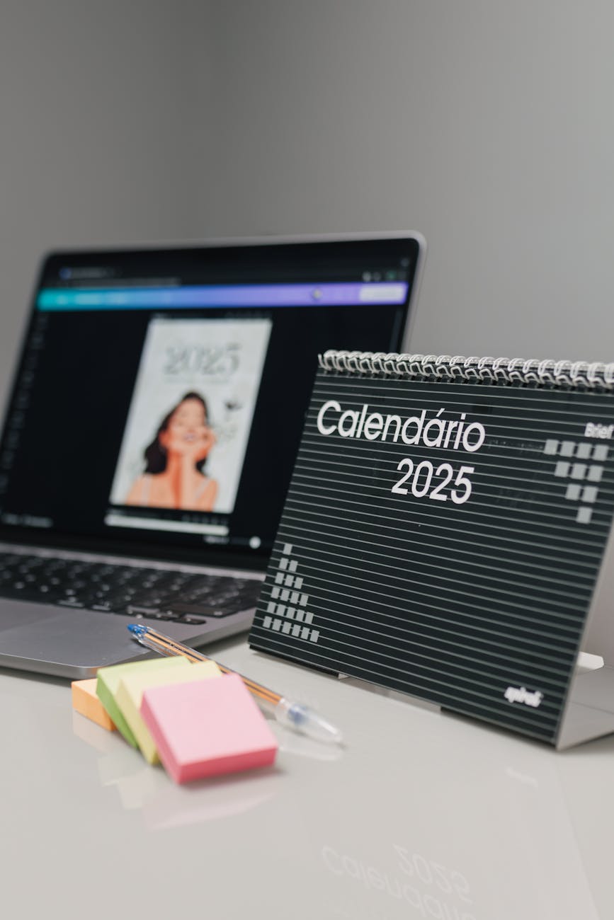 A desk setup featuring a 2025 calendar, laptop screen showing digital design, and sticky notes.