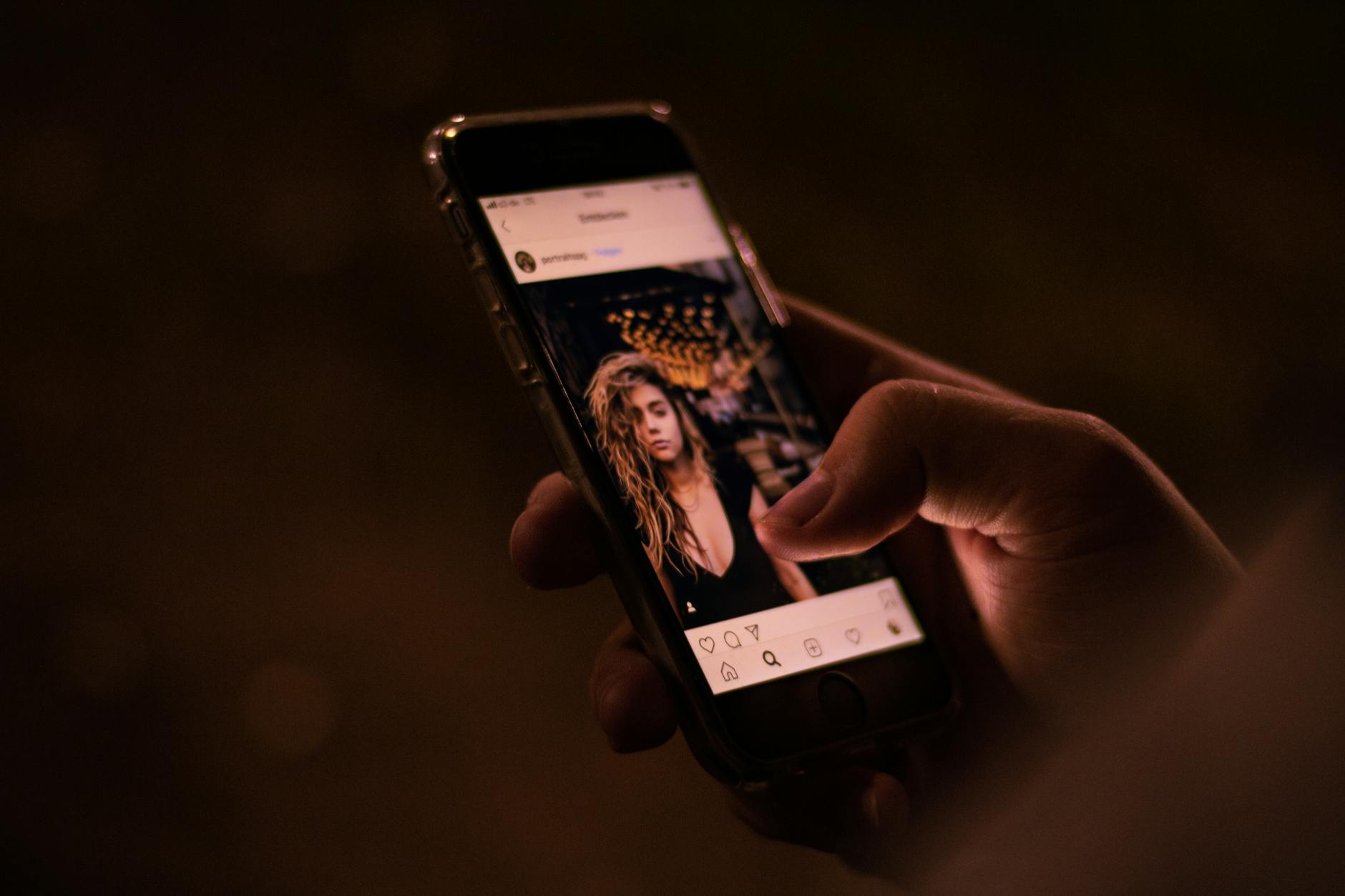 Close-up of a hand interacting with a smartphone, browsing social media at night.
