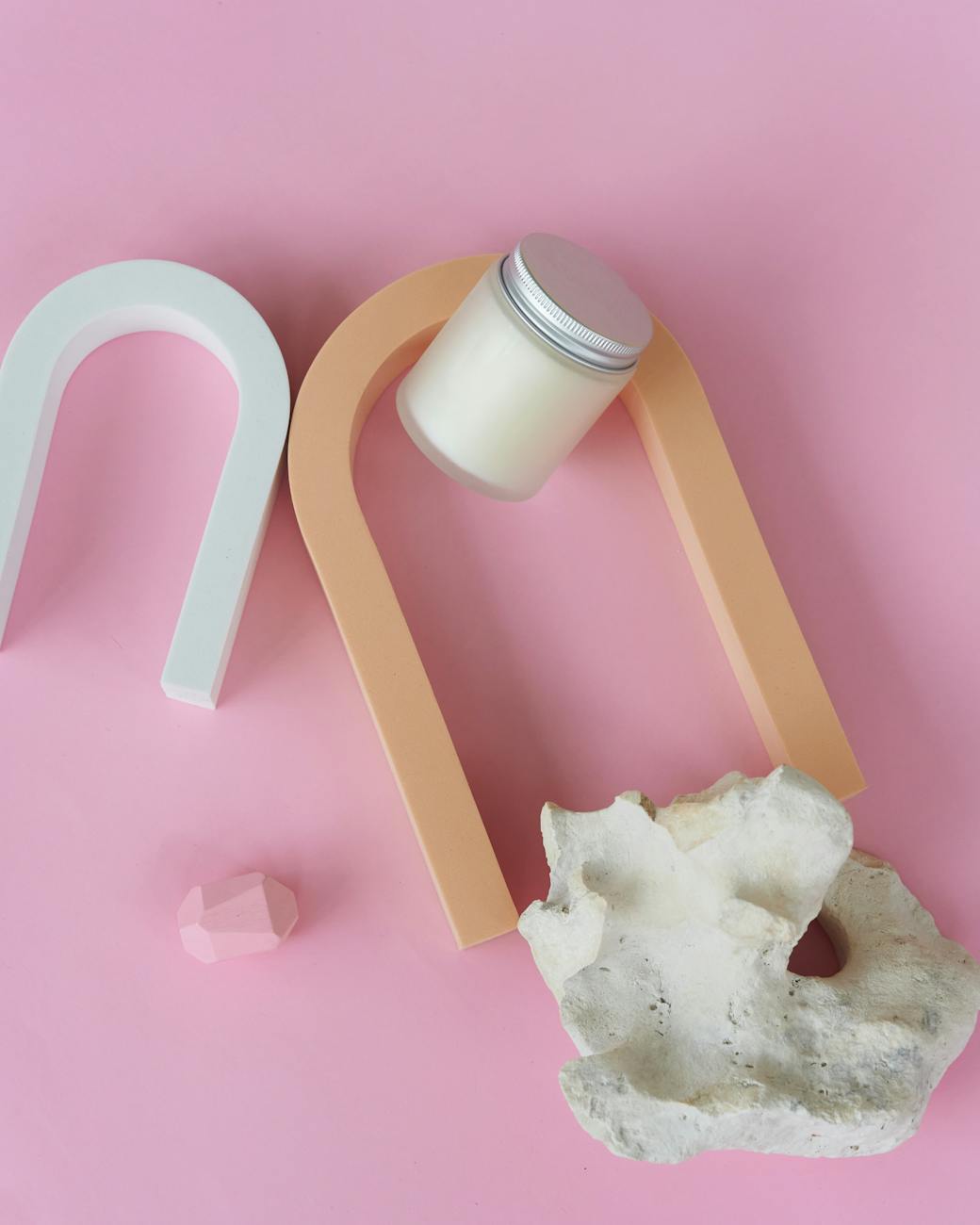 Aesthetic composition with candle, arches, and coral on pink backdrop.