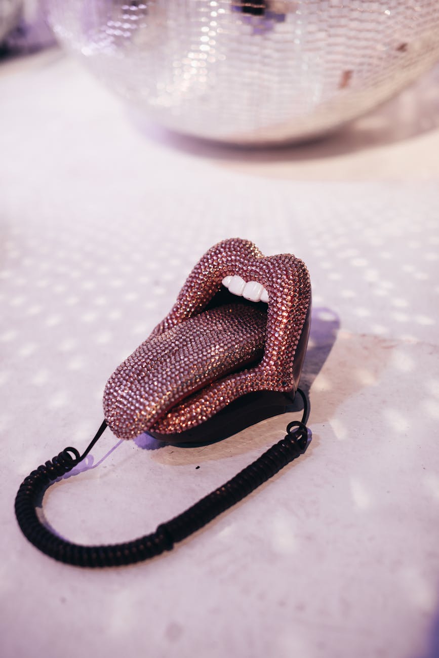 Stylish retro lip-shaped telephone on dancefloor with disco ball reflections.