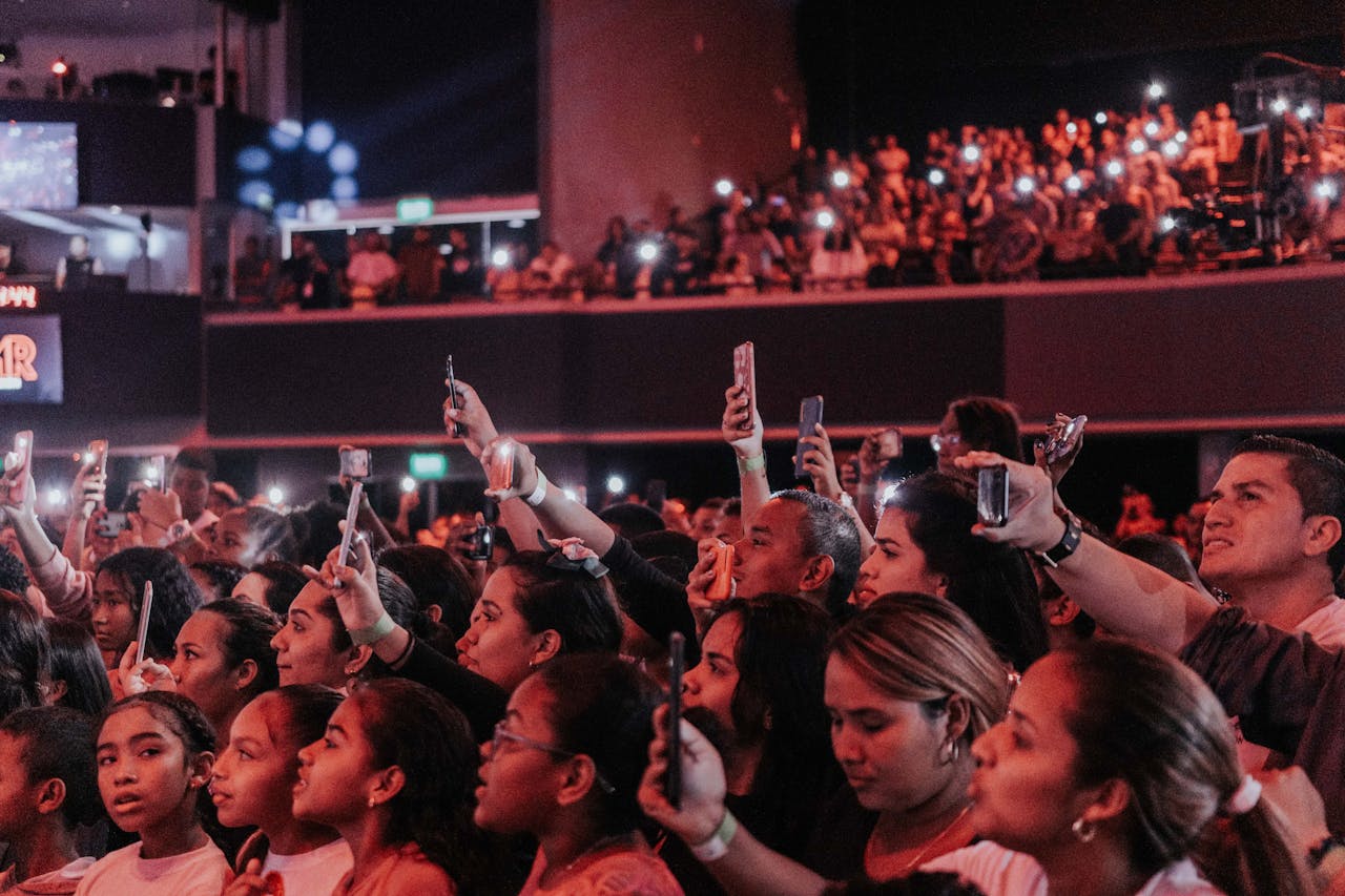 Lively audience enjoying a concert, capturing moments with smartphones in a vibrant atmosphere.