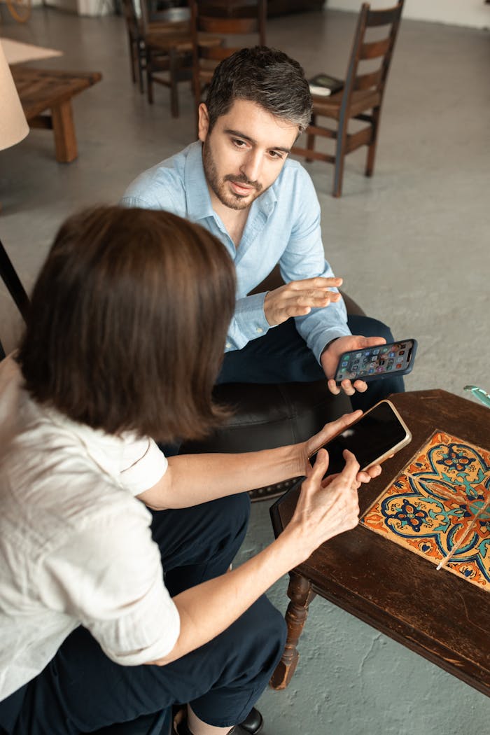 Two adults sitting and discussing something on smartphones indoors, focused interaction.