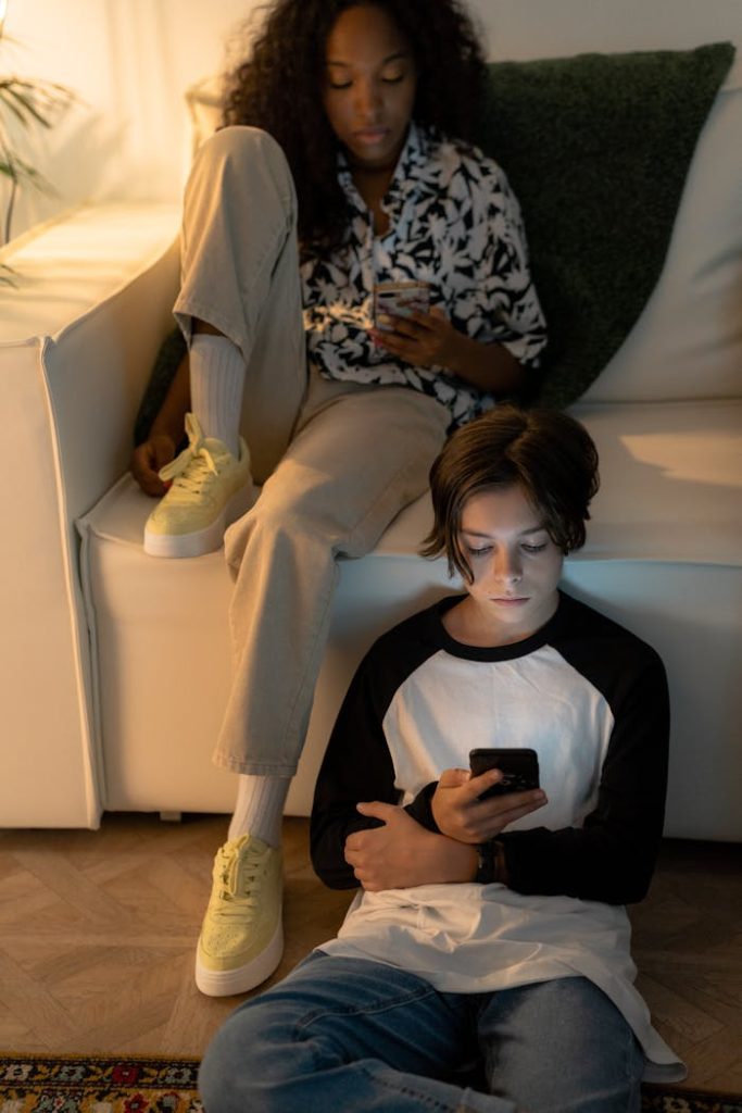 A black girl and caucasian boy using smartphones in a cozy living room setting.