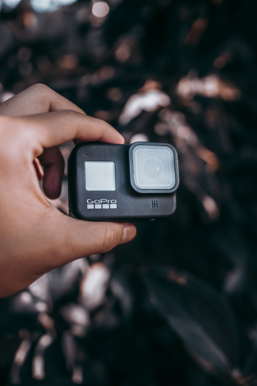 Focused shot of a hand holding a GoPro camera against a blurred dark background, suitable for adventure concepts.