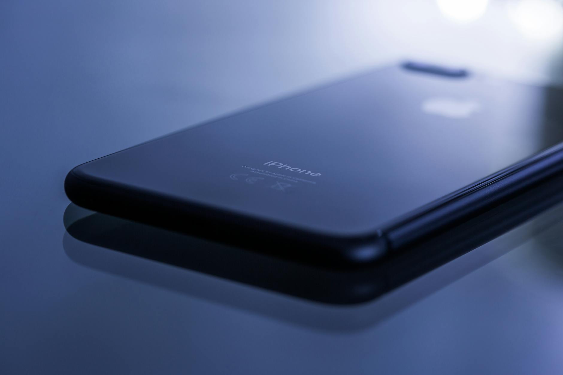 Minimalist photo of a glossy smartphone on a reflective surface, highlighting its sleek design.