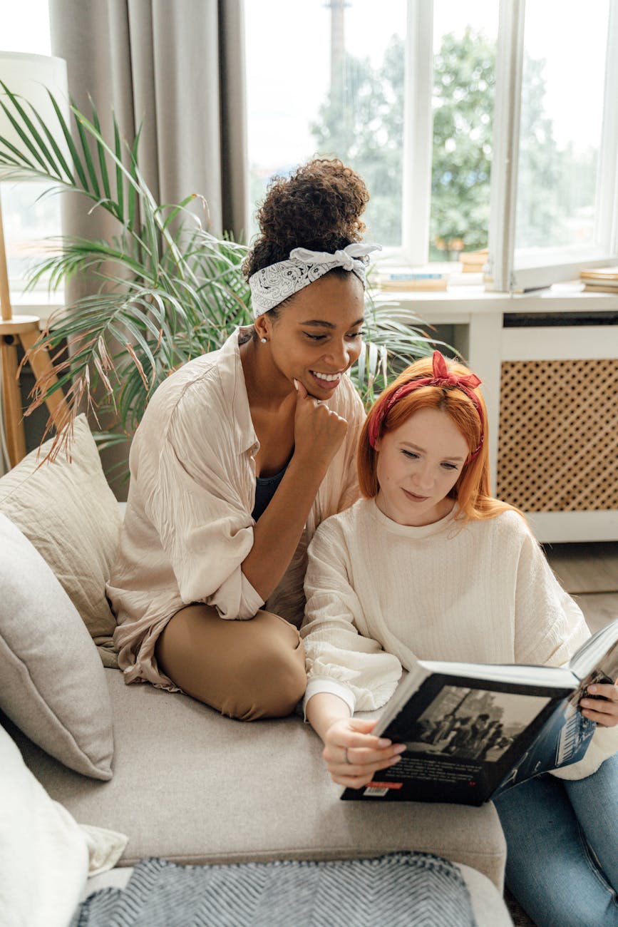 Two friends enjoy a cozy day indoors, sharing a moment over a book and conversation.