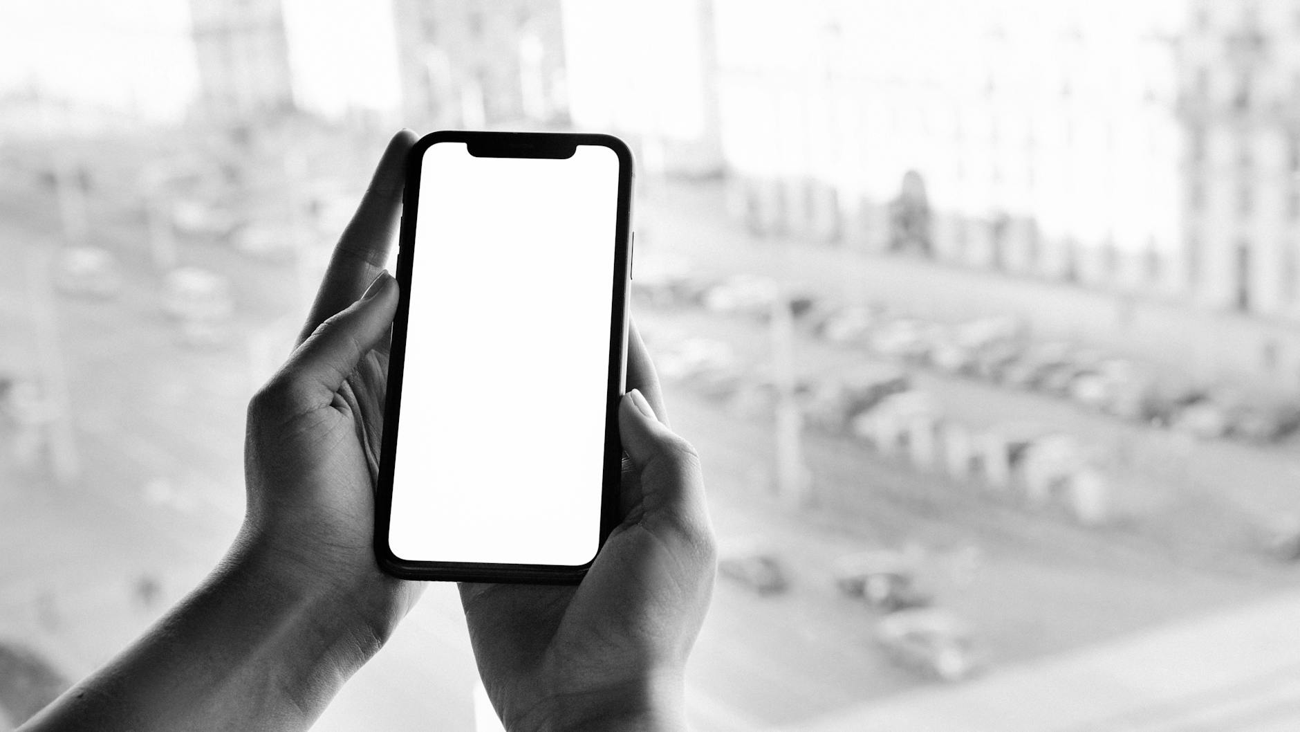 Black and white image of hands holding a smartphone with a blank screen, outdoor city view.