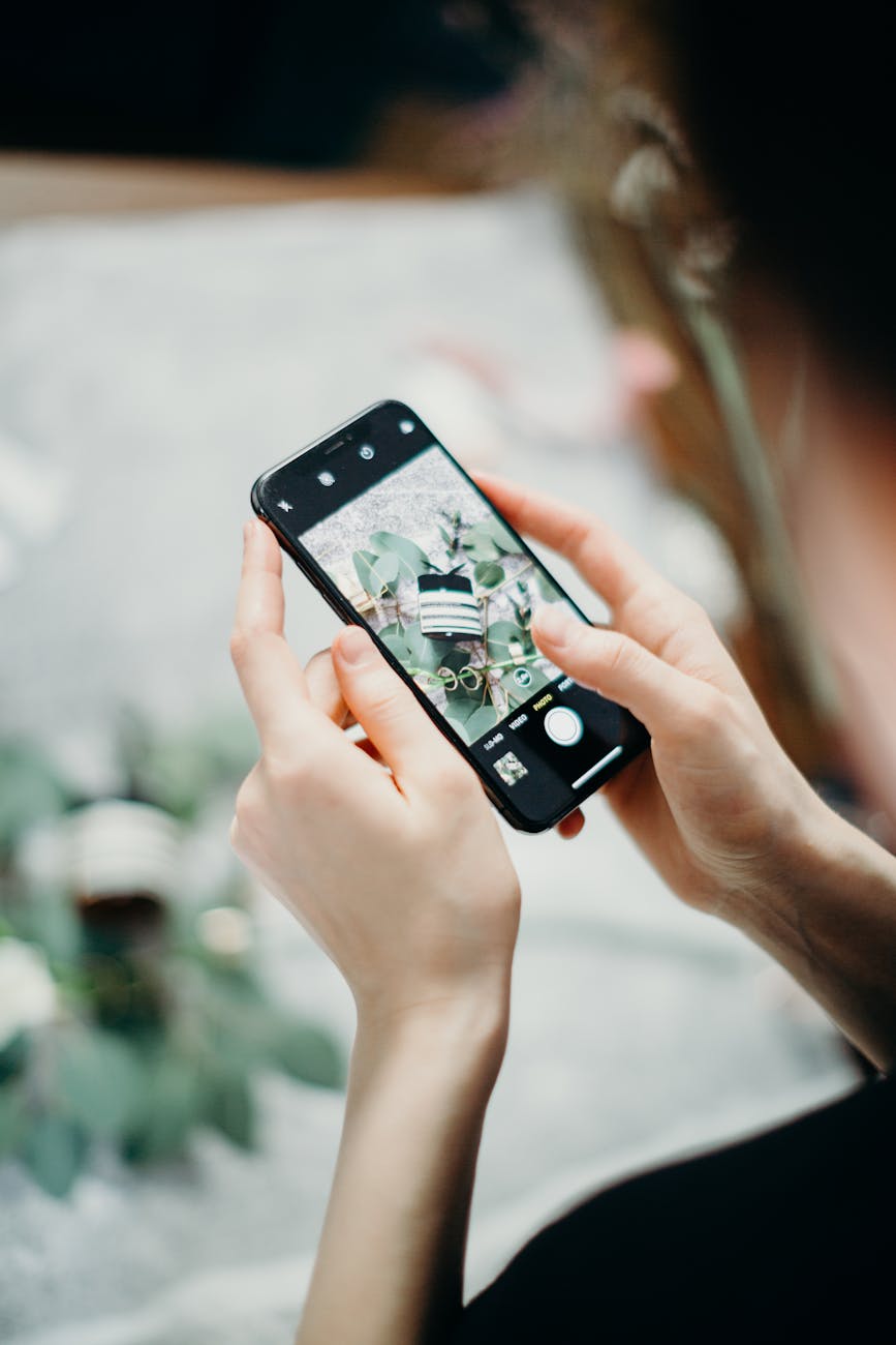 Photo of a person using a smartphone to capture a bouquet of flowers, indoors with natural lighting.