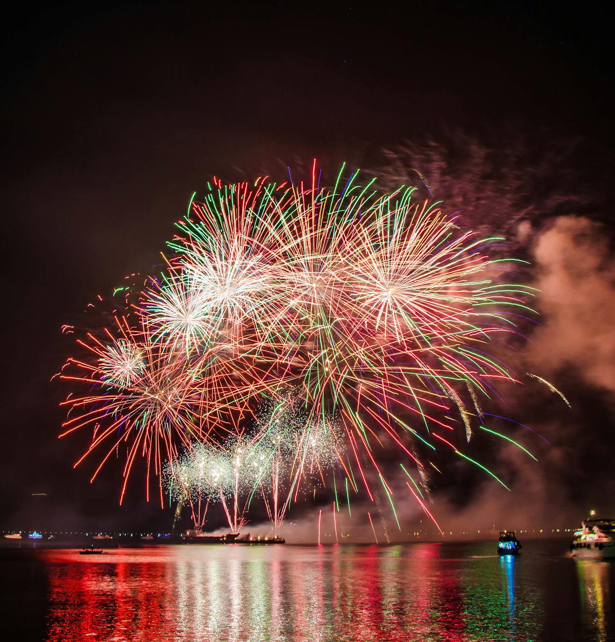 Colorful fireworks illuminating the night sky above a serene water body, creating a festive atmosphere.